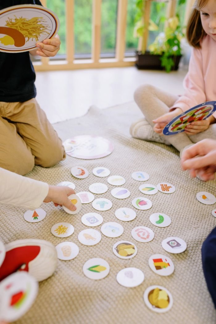 Three children engage in a fun card game while seated on a rug indoors, promoting learning and interaction.